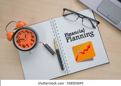 Business management concept (financial planning), note book, computer, glasses and vintage alarm clock on wooden table
