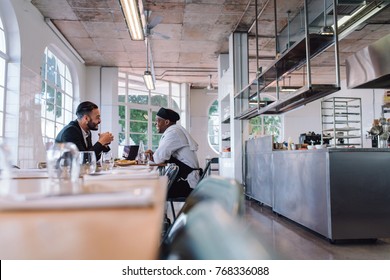 Business manager and chef talking in restaurant. Restaurant owner and cook sitting at table and having conversation.