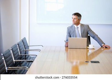 Business Manager Sitting At The End Of A Meeting Table, With Cup Of Cafe And Laptop.