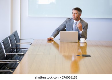 Business Manager Sitting At The End Of A Meeting Table, With Cup Of Cafe And Laptop.