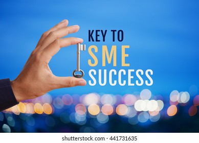 Business man's hand holding and raising key with word Key to SME SUCCESS on abstract twilight bokeh night scene background. Business concept of key to SME success. 
