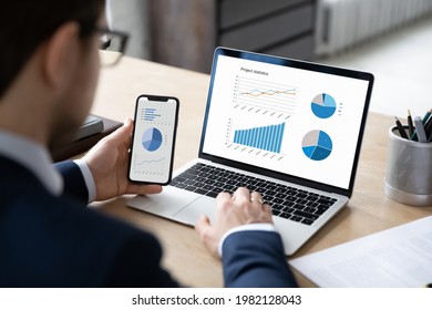 Business marketer using professional app for marketing data analyzing on laptop and smartphone screens, studying financial graphs, comparing diagrams on phone and computer. Analysis concept