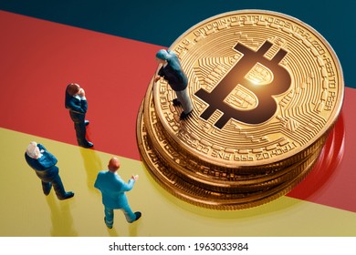 Business meeting about the investment decision for bitcoin concept: Miniature businessman figurines standing near the pile of shiny golden bitcoin on Germany flag.