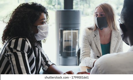 Business Meeting With Coronavirus Safety Measures. Young Multiethnic Colleagues Talk At Office Table Wearing Face Masks.