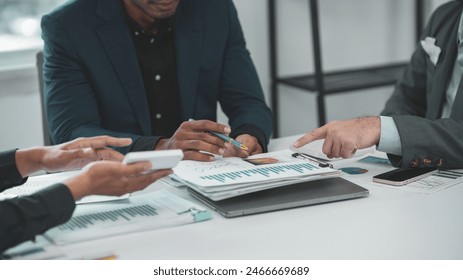 Business meeting with diverse team discussing charts and graphs on table with devices, papers, and modern office environment. - Powered by Shutterstock