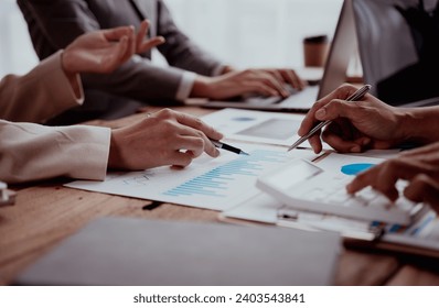 Business meeting with hands pointing at financial charts and a laptop on a wooden table. - Powered by Shutterstock