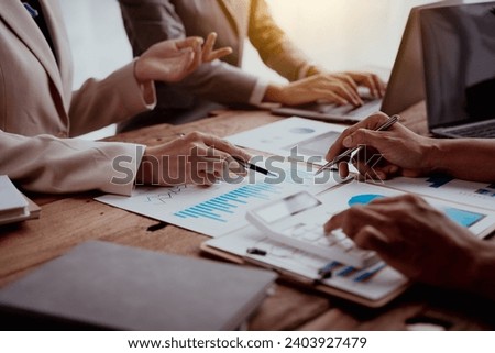 Business meeting with hands pointing at financial charts and a laptop on a wooden table.