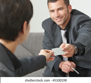 Business Meeting At Office Lobby, People Sitting On Sofa Changing Business Cards. Focus On Card.