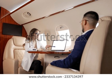 business meeting on airplane, business woman in suit and glasses discusses deal with client and points to laptop screen, business people fly in private jet and work Foto stock © 
