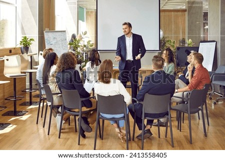 Business meeting. Serious business group leader instructing team, telling project strategy and presenting tasks. Confident man is talking to colleagues sitting in circle at meeting in office.