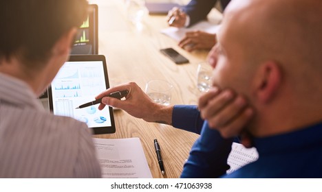 Business Meeting Taking Place With Diverse Group Of Business People In A Modern Office With Several Electronic Devices At Their Aid, Including The Tablet Being Held By One Of The Executives.