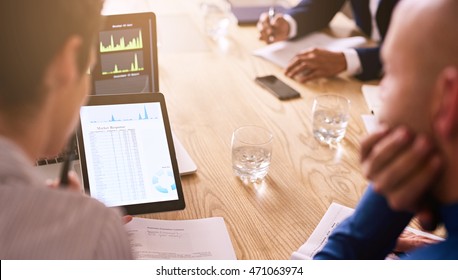 Business Meeting Taking Place With Diverse Group Of Business People In A Modern Office With Several Electronic Devices At Their Aid, Including The Tablet Being Held By One Of The Executives.