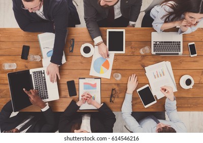 Business Meeting Top View. Busy People Work In Office, Above View Of Wooden Table With Mobile Phones, Laptop, Tablet And Documents Papers With Diagram.