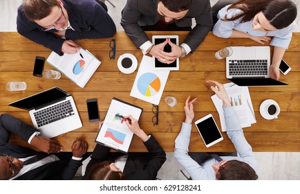 Business Meeting Top View. Busy People Work In Office, Above View Of Wooden Table With Mobile Phones, Laptop, Tablet And Documents Papers With Diagram.