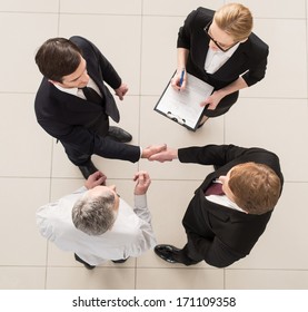 Business Meeting. Top View Of Four People In Formalwear Standing Close To Each Other While Two Of Them Handshaking