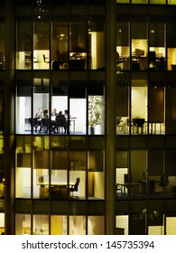 Business Meeting Viewed Through Illuminated Window Of Office Block At Night