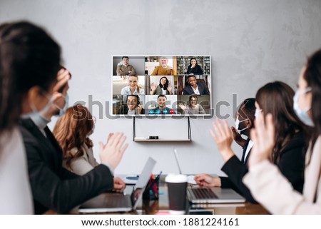 Business meeting.A group of formal successful people wearing protective masks sit at the table and communicate online via videoconference with colleagues discussing about important business strategies