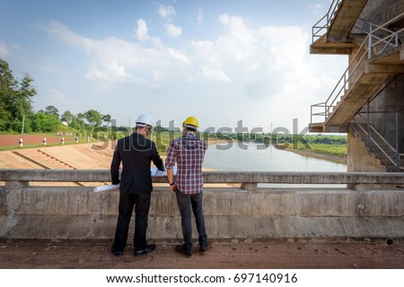 Business men meeting with Engineers and supervisors are standing reading the blueprints at the construction site.