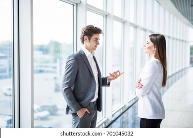 Business Men And Women Talking With A Smile On The Background Of The Large Panoramic Windows In A Modern Business Center.