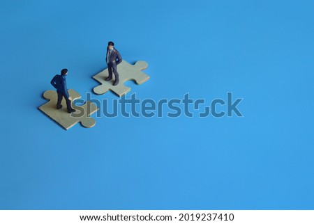 Business mergers and acquisitions, partnership concept. Two miniature people merging on puzzle. Copy space for text