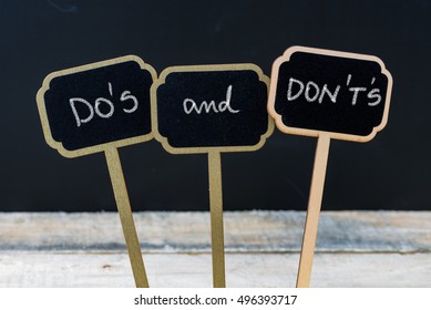Business message DO'S and DON'T'S written with chalk on wooden mini blackboard labels, defocused chalkboard and wood table in background