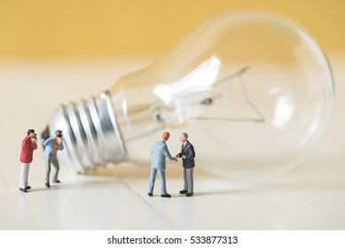 Business Miniature People Make Handshaking Agreement With Light Bulb Background