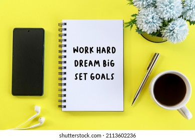 Business Monday Motivational Words - Work Hard, Dream Big, Set Goals. With Text Message Write On A Book, A Cup Of Morning Black Coffee, Pen, Earphone, Blue Flowers On Yellow Table Top View Background.