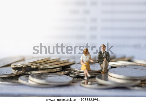 Business and money concept. Businessman and\
female miniature figure sitting and talking on stack of coins with\
bank passbook as\
background.