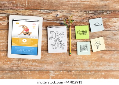 business, multimedia, objects and technology concept - close up of notebook, tablet pc computer with fitness application and stickers on table