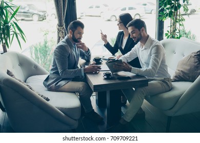 Business Negotiation In A Cafe. Three Partners Are Discussing The Contract. Young Bearded Attractive Brunet In A Formal Wear Is Reporting, Showing On A Pda`s Monitor, Lady Is Browsing Data On Phone