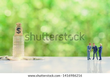 Business negotiation, top management team share vision together : Miniature figurine CEO CFO CMO discuss / talk or brainstorming on company future income / revenue project with dollar bag on coins. 