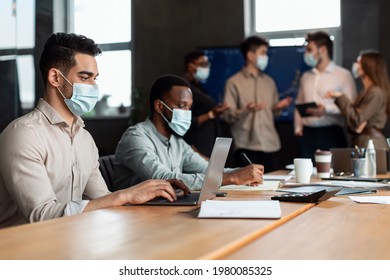 Business And New Normal Concept. Team Of Young Diverse Programmers Working In Software Developing Company, Typing On Laptops, Testing New Games Or Apps, Wearing Medical Masks, Sitting At Desk