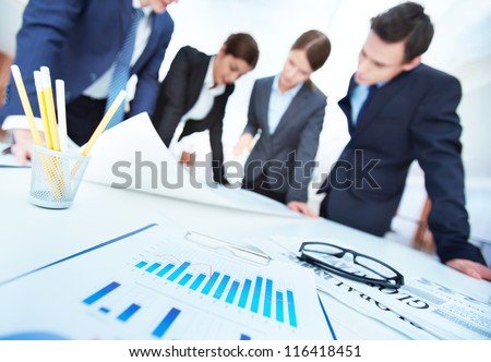 Business objects on background of engineers discussing blueprint at meeting