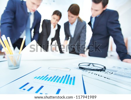 Business objects on background of engineers discussing blueprint at meeting