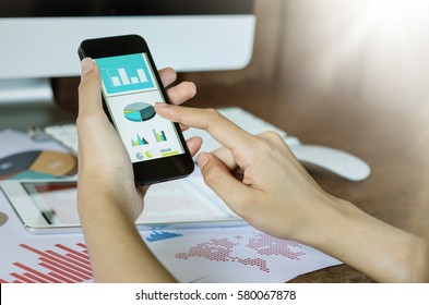 Business, office concept. Woman's hands using smart phone with financial document.