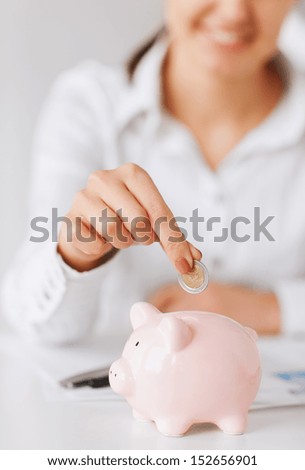 business, office, household, school, tax and education concept - woman hand putting coin into small piggy bank