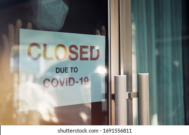 Business office or store shop is closed, bankrupt business due to the effect of novel Coronavirus (COVID-19) pandemic. Unidentified person wearing mask hanging closed sign in background on front door. - Shutterstock ID 1691556811