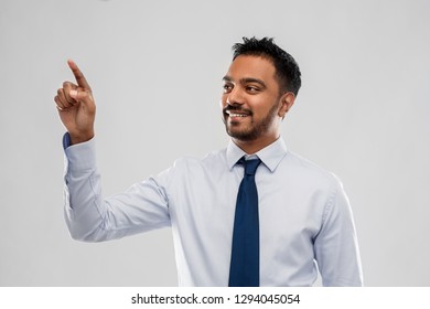 business, office worker and people concept - smiling indian businessman touching something invisible or working with virtual screen over grey background - Powered by Shutterstock