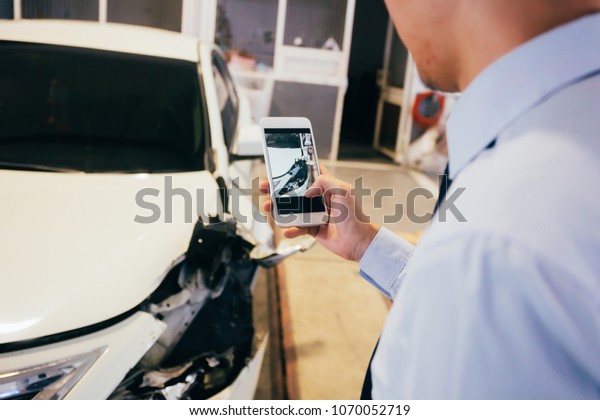 Business officer taking a photo of damaged and\
wrecked car bender in garage as evidence for insurance and\
verification purpose