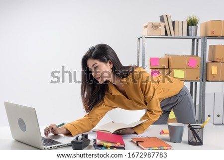 In business on line,e-commerce,plenty of post box on shelf and paper schedule on table.Young beautiful entrepreneur woman,teenager business owner prepare mail to customer.
