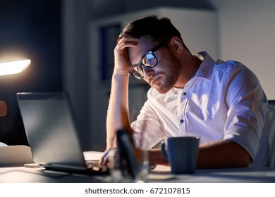 business, overwork, people, deadline and technology concept - stressed businessman in glasses with laptop computer thinking at night office
