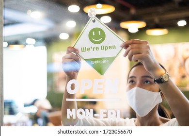 Business Owner Asian Woman Wear Protective Face Mask Ppe Hanging Open Sign At Her Restaurant / Café, Open Again After Lock Down Due To Outbreak Of Coronavirus Covid-19