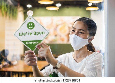 Business owner Asian woman wear protective face mask ppe hanging open sign at her restaurant / café, open again after lock down due to outbreak of coronavirus covid-19 - Shutterstock ID 1728718951
