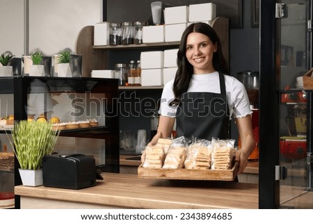 Business owner in her cafe. Happy woman holding tray with delicious pastries at desk