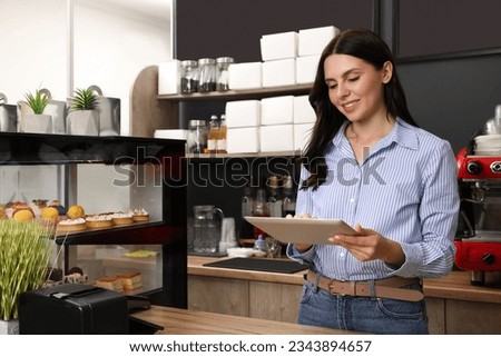 Business owner in her cafe. Woman using tablet near showcase with pastries