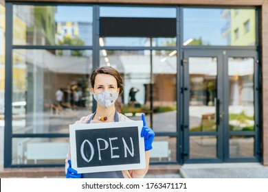 Business owner Hispanic woman wear protective face mask holding open sign at her at her zero waste grocery shop outdoor. Business open again after coronavirus covid-19. Supporting local business. - Powered by Shutterstock