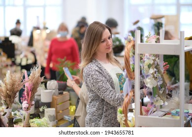 business owner selling behind counter with her bouquet of dried flowers at local market of craftsmen, small business. young woman entrepreneur sells floral holiday composition.