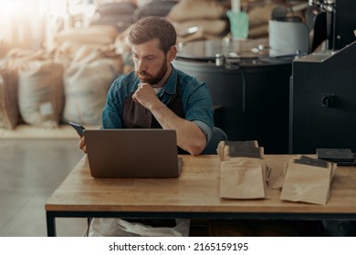 Business Owner Of Small Coffee Roasting Factory Working On His Workplace Using Laptop And Phone