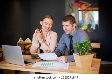 Business owners of small modern cafe discussing paperwork at table - Young smiling woman looking at finance with team man partner over a coffee – teamwork meeting to analyze financial data and profit - Powered by Shutterstock