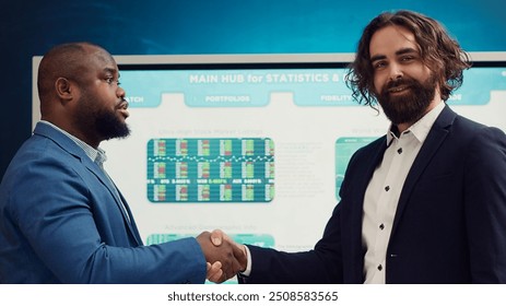 Business partners celebrate the beginning of a new project between their companies, shaking hands in a meeting. Leaders forging an agreement to develop the corporation and collect resources. Camera A. - Powered by Shutterstock